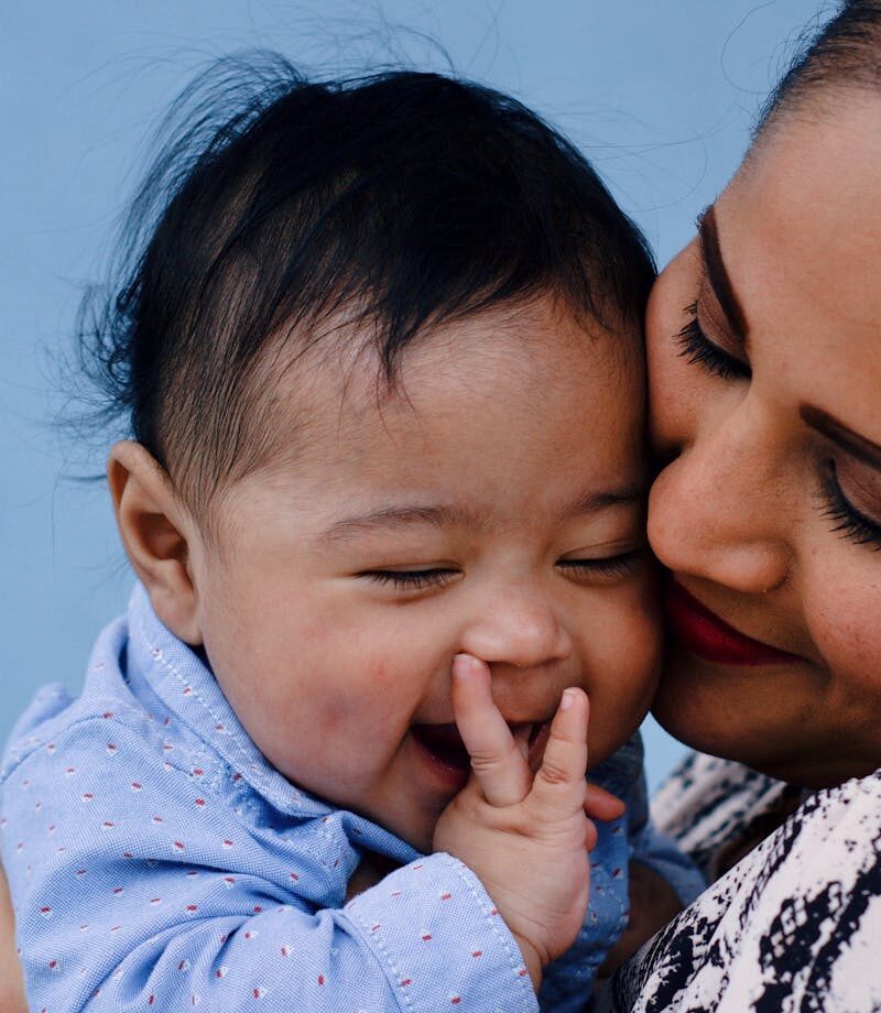 pexels-photo-3766464-3766464 A mother affectionately embraces her baby against a serene blue background.