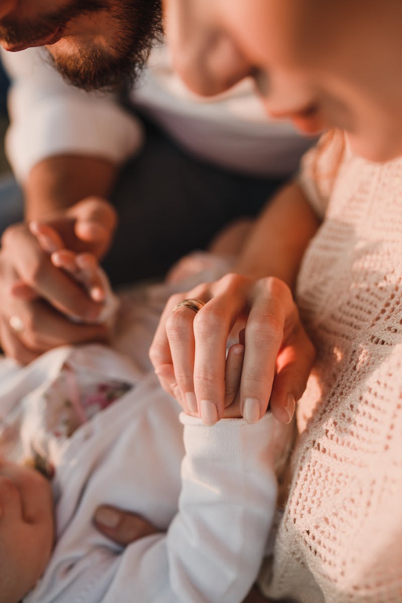 pexels-photo-5416643-5416643 Close-up of parents holding their baby's hand in a warm, intimate setting.