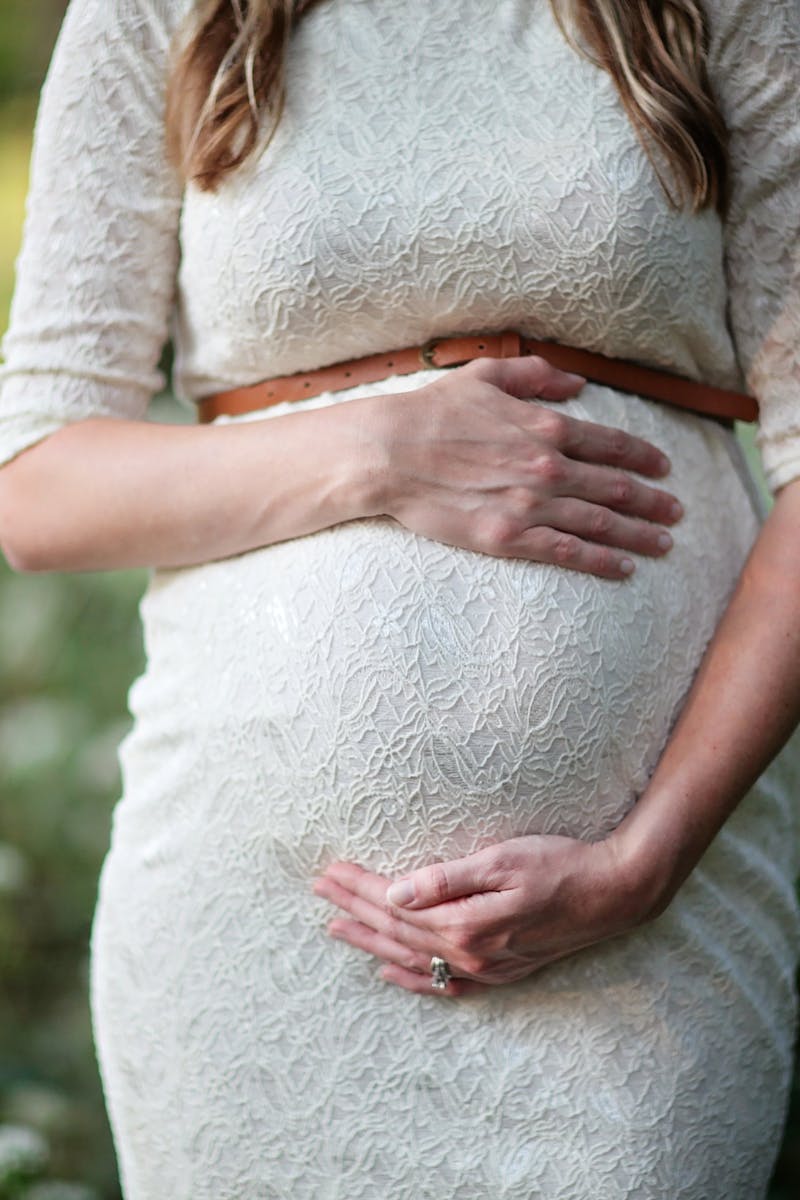 pexels-photo-618923-618923 A pregnant woman in a lace dress gently cradling her belly in an outdoor setting.