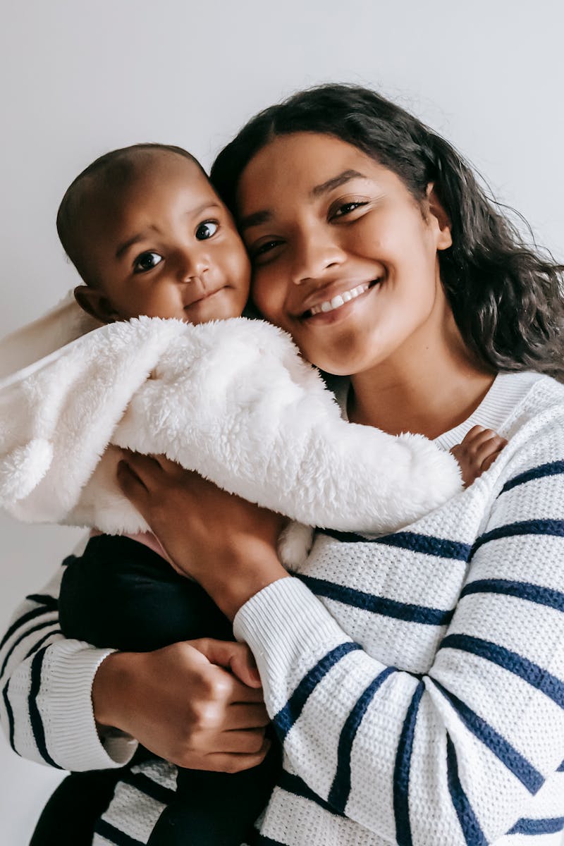 pexels-photo-6393377-6393377 A joyful mother holds her smiling baby in a cozy indoor setting.