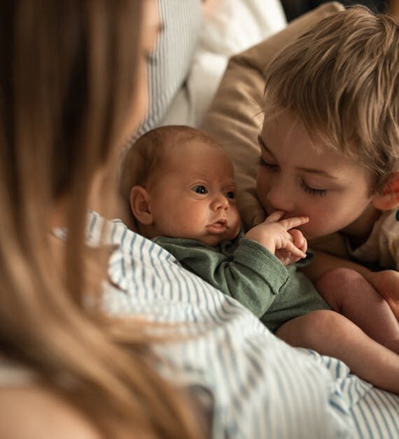 pexels-photo-6849558-6849558 A heartwarming moment as a young child embraces a newborn sibling with mother nearby.